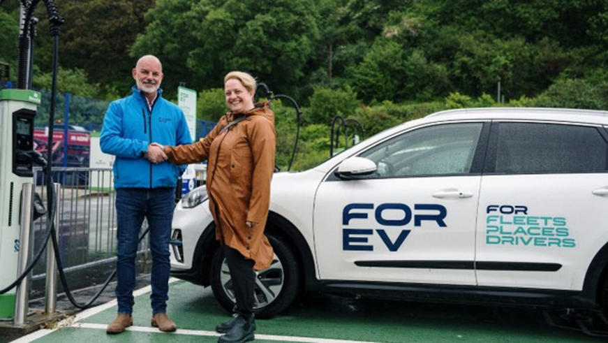 Two people shaking hands next to an electric vehicle charger