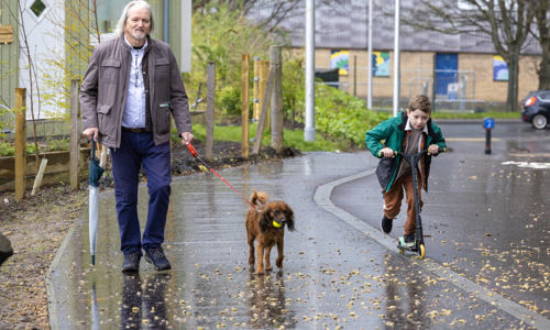 Person walking a dog, with a child on a scooter alongside