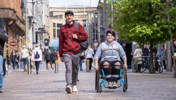 A person walking with a wheelchair user on Buchanan St in Glasgow